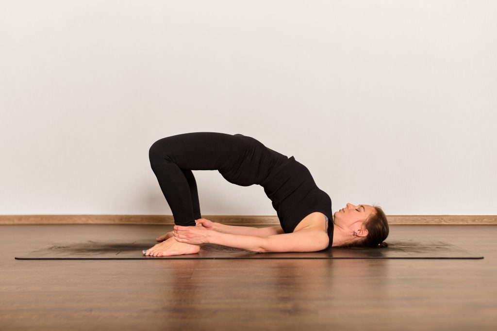 An individual practices the yoga bridge pose on a mat, serene studio backdrop. 