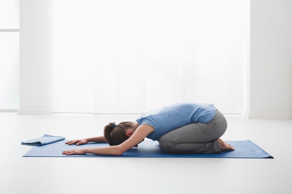 A woman practicing the yoga child's pose and meditation at home on the floor, she is kneeling on the floor and bending, half tortoise pose