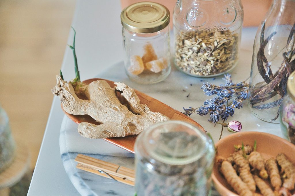 A marble tray for cozymoodallday.com holds dried ginger root, glass jars with dried herbs and sugar cubes, a sprig of lavender, and wooden clothespins—perfect props for an article about ginger shots for health and skin care.