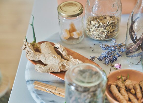 A marble tray for cozymoodallday.com holds dried ginger root, glass jars with dried herbs and sugar cubes, a sprig of lavender, and wooden clothespins—perfect props for an article about ginger shots for health and skin care.