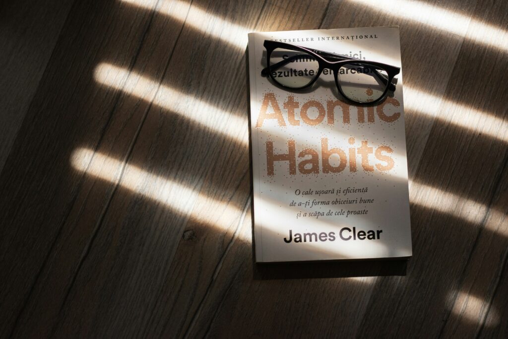 Life-Changing Healthy Habits book “Atomic Habits” by James Clear with glasses on a wooden surface in natural light