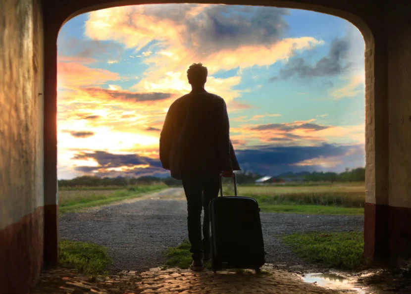 Benefits of travelling shown by a solo traveler with luggage walking toward a peaceful sunset countryside road.
