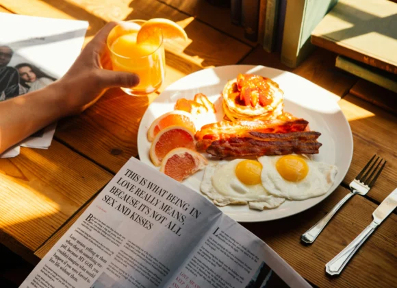 Alt text: High-protein breakfast with fried eggs, crispy bacon, pancakes topped with strawberries, fresh grapefruit slices, and a glass of orange juice on a wooden table.