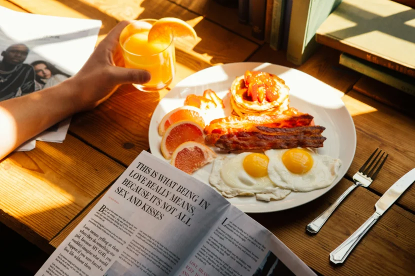 Alt text: High-protein breakfast with fried eggs, crispy bacon, pancakes topped with strawberries, fresh grapefruit slices, and a glass of orange juice on a wooden table.