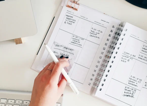 Woman writing tasks in a weekly agenda notebook as a daily planning and time management strategy to stay productive.