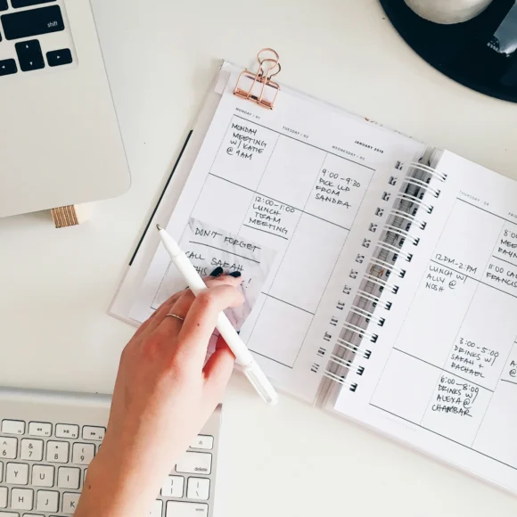 Woman writing tasks in a weekly agenda notebook as a daily planning and time management strategy to stay productive.